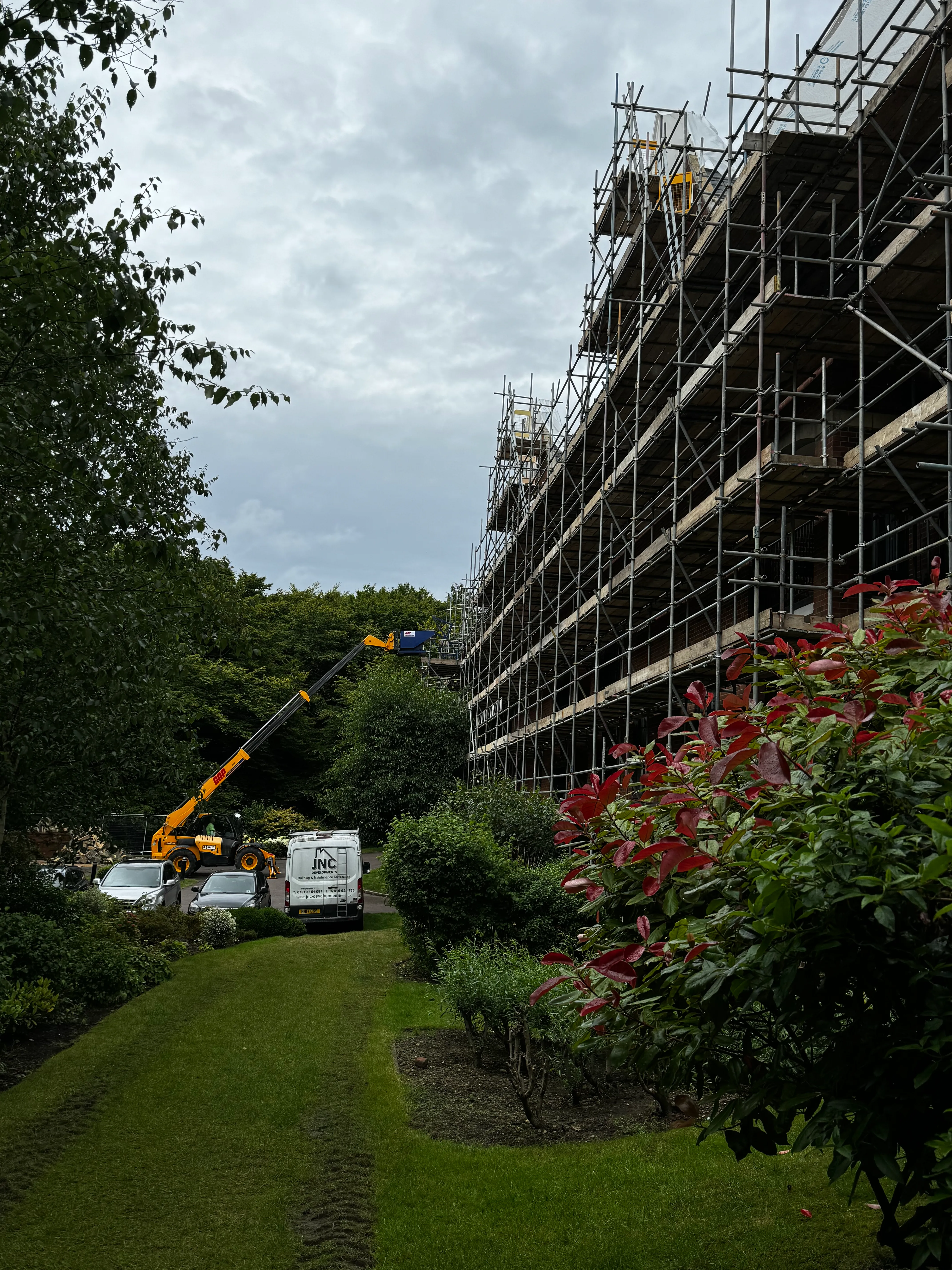 Scaffolded elevation of a stone building with a crane and site vehicles