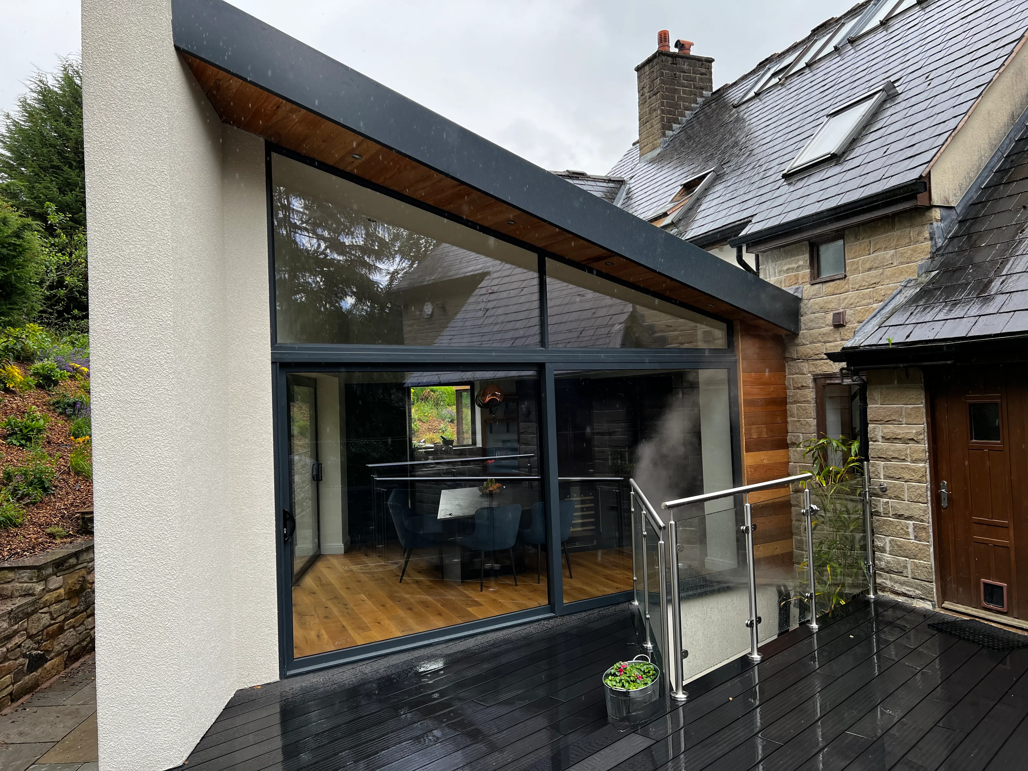 Cedar-clad extension with sliding glazing and a composite deck on a wet evening