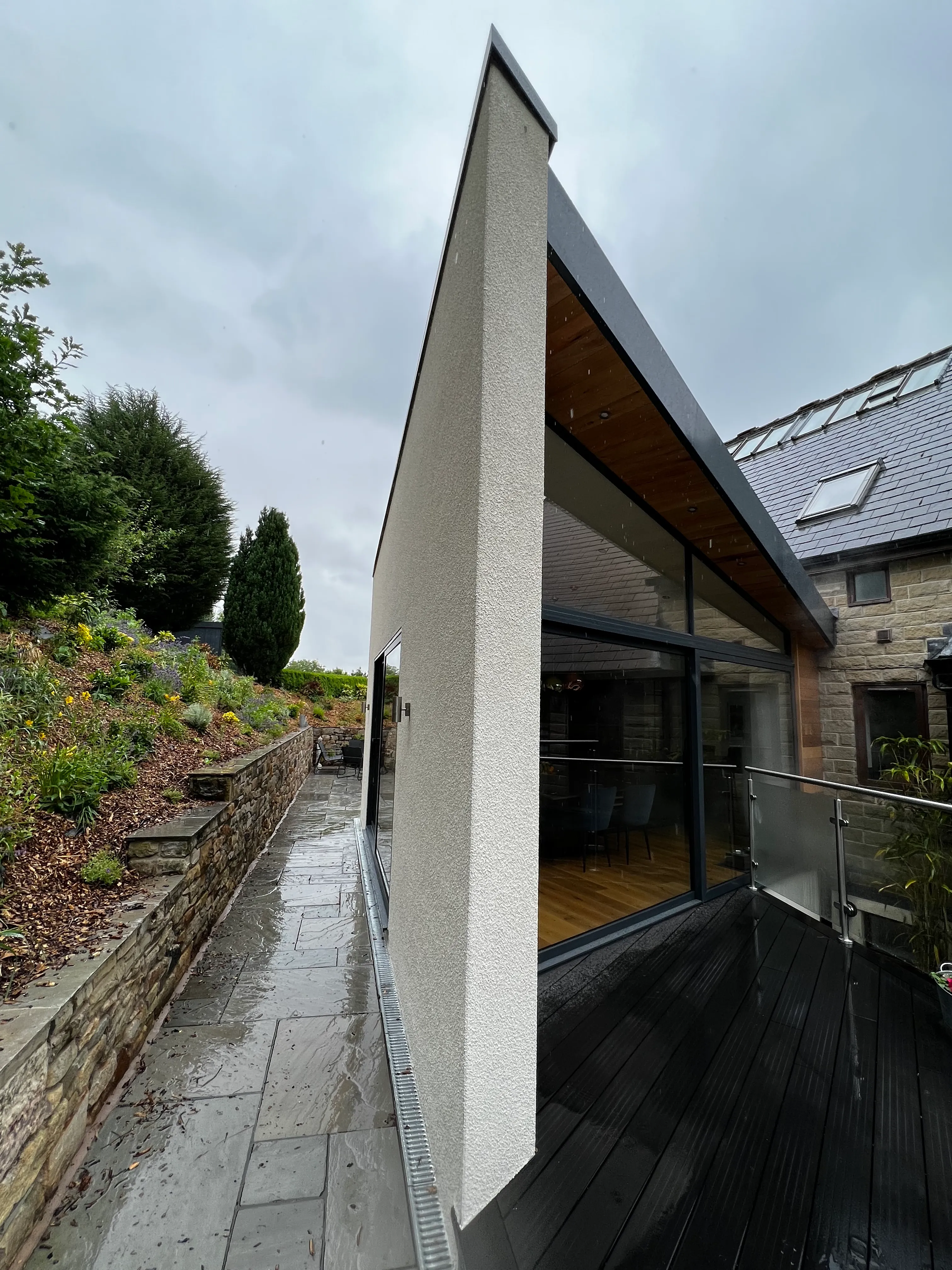 Rendered extension with cedar soffit beside a stone house