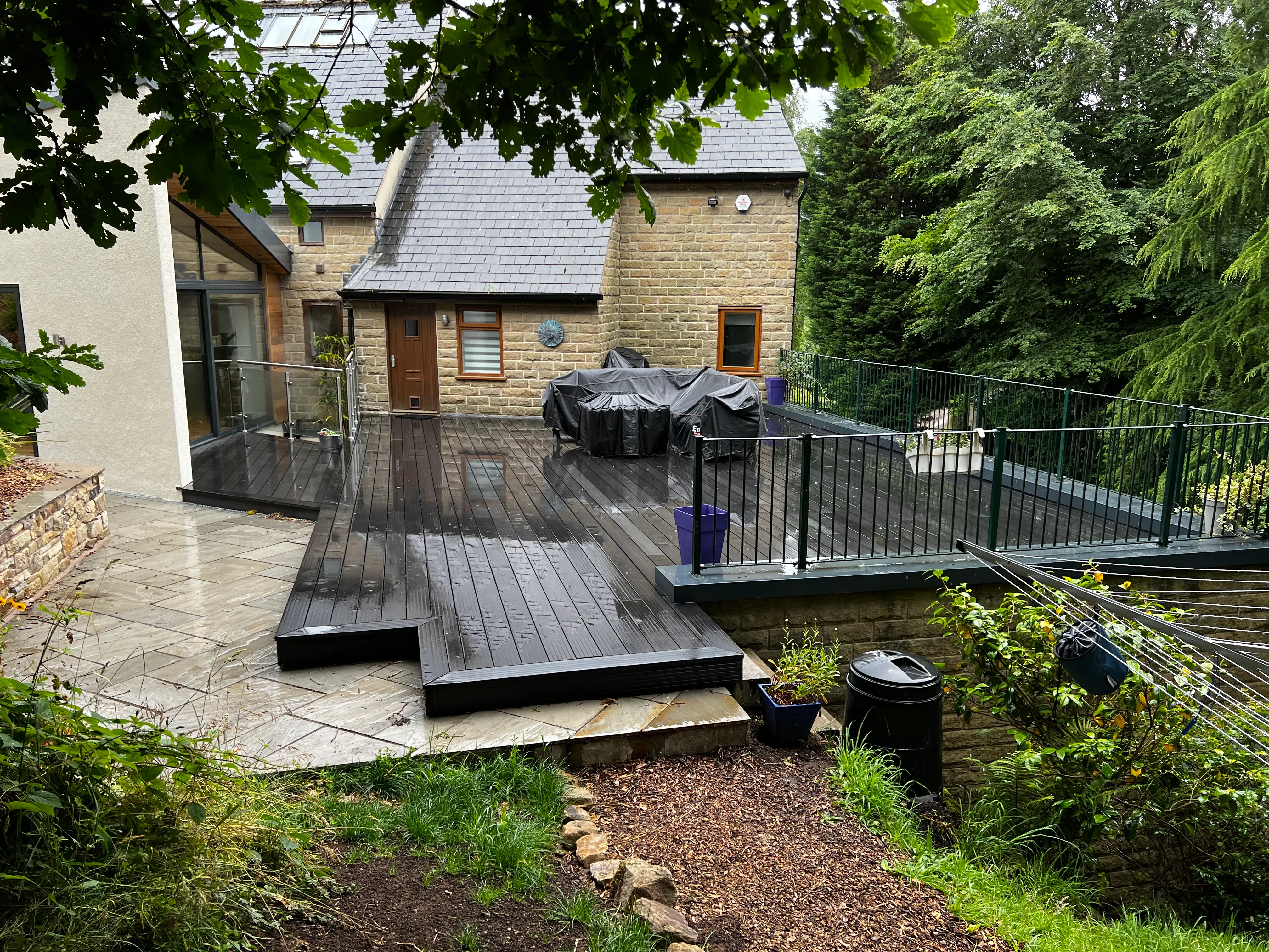 Composite deck and glass balustrade beside a stone house and rendered extension